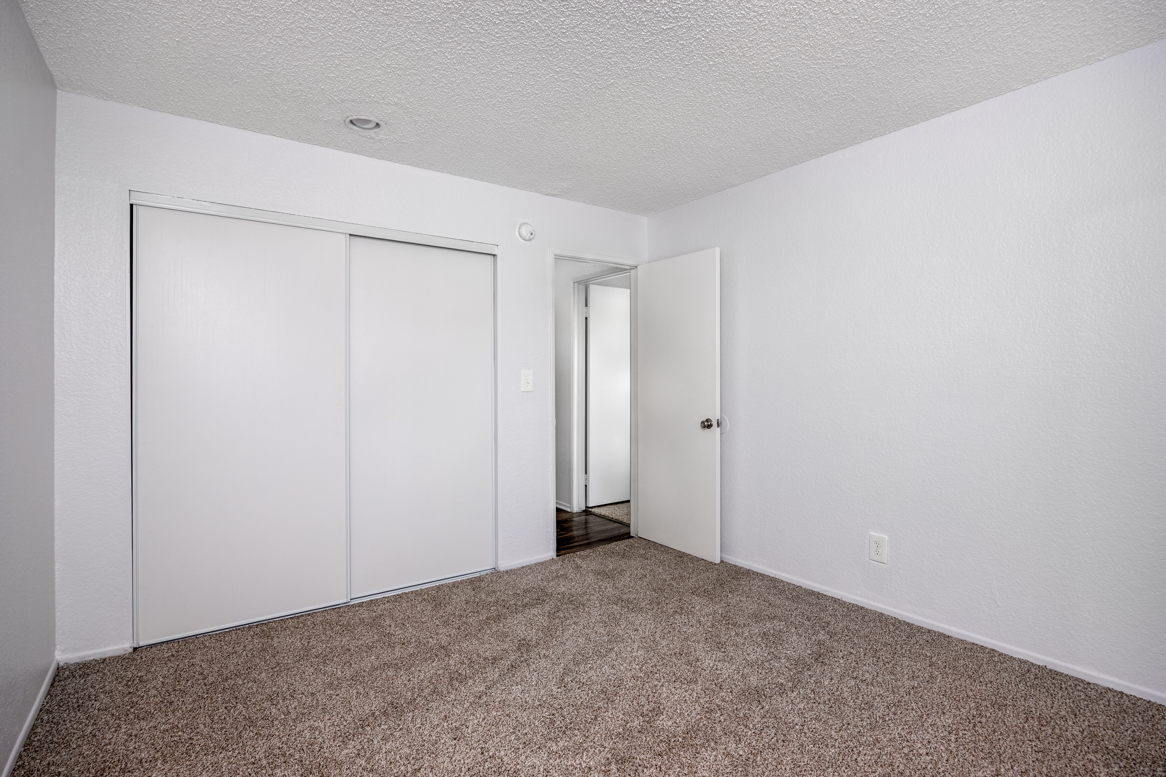 A room with carpeted floor and white walls with a door and a closet.